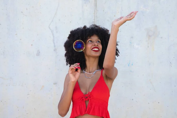 Beautiful afro american woman playing with soap bubbles. The woman is blowing the bubbles and hides among the soap bubbles. Happiness concept