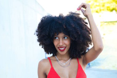 Güzel Afro-Amerikan kadın gülümseyen ve kameraya bakan farklı pozlar veren ve yüzüyle jestler yapan. Kadın kırmızı bir üst ve kırmızı bir ruj sürüyor. Mutluluk kavramı