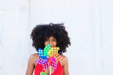 Young and beautiful Afro-American woman holds a windmill in her hands and is spinning it with the air from her lips. Summer concept and colour
