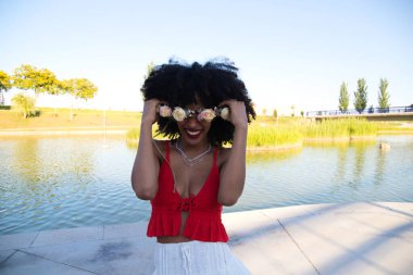 beautiful young afro american woman doing different poses and gestures on camera. She wears in her hair a crown of pink flowers and a red top. Lifestyle concept