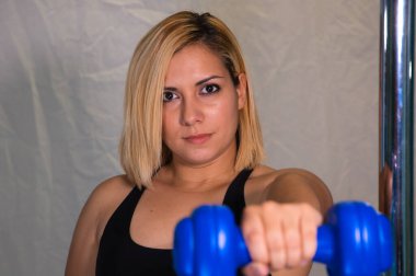 Spor salonunda elinde mavi bir dambıl tutan güzel sarışın bir kadının eli. Jimnastik konsepti sağlıklıdır. Tombul ve kıvrımlı kadın..