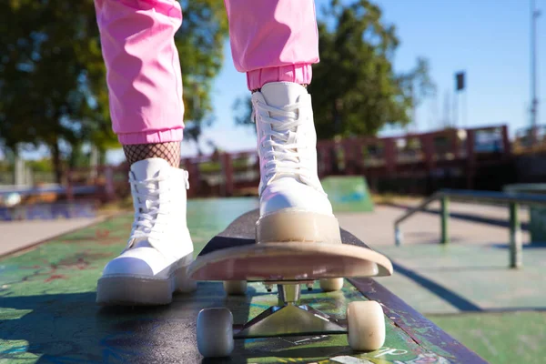 一个女孩在滑板上的脚的细节 这个女孩穿着粉红色的裤子和白色的靴子 这是一个阳光灿烂的日子 — 图库照片