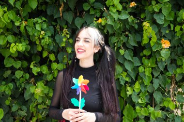 Punk tarzı güzel bir genç kadın elinde renkli bir yel değirmeni tutuyor. O, gülümseyen kameraya bakıyor. Yaz, hava.