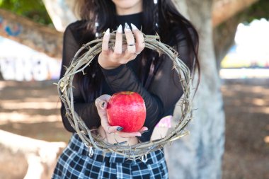 punky girl holding a red apple and a crown of thorns in her hands. represents the apocalypse from the beginning with adam and eve. The girl is gothic with blonde and brown hair. clipart