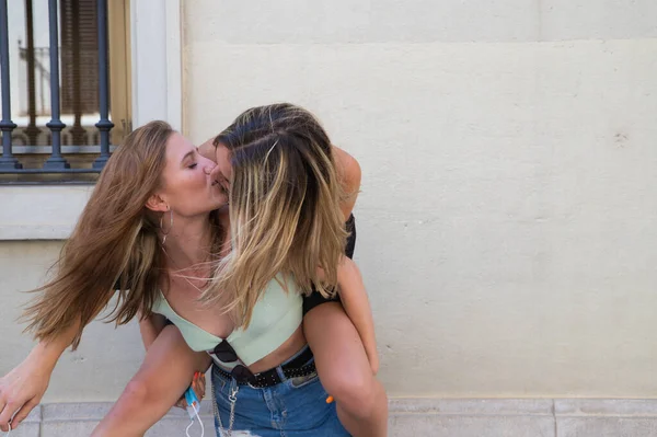 two beautiful young women on holiday. The women are lesbians and one is carrying the other. They are kissing because they are a couple. Concept of equality and diversity.