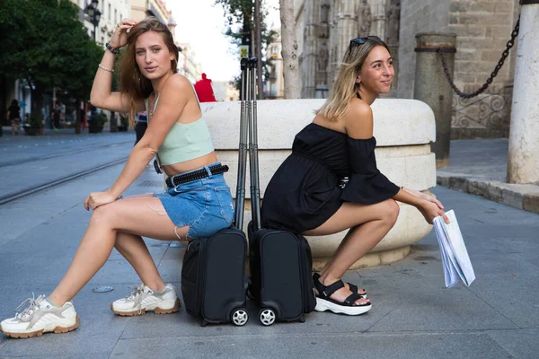 市内の2人の若いと美しい女性観光 女の子はスーツケースの上に座っている 非常に幸せと笑みを浮かべてポーズ 彼らは地図とカメラを持っている 休暇と旅行のコンセプト — ストック写真