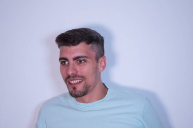 Beyaz arka plandaki genç adam profilden bakıyor ve gülümsüyor. Mutluluk ve ifadeleri kavra.