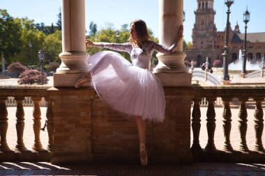 Beyaz etekli klasik balerin dans ediyor ve iki beyaz mermer kolona tutunuyor. Kadın dans ederken sütunlarla flört ediyor. Dans konsepti