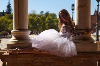 Beyaz etekli klasik balerin dans ediyor ve iki beyaz mermer kolona tutunuyor. Kadın dans ederken sütunlarla flört ediyor. Dans konsepti