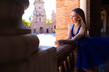 Tavus kuşu mavisi etekli klasik balerin korkuluğa eğilip ufka bakıyor. Balerin güzel ve genç. Klasik bale konsepti.