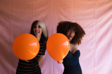 İki kadın, biri sarışın, diğeri Afro-Amerikalı, genç ve güzel, Cadılar Bayramı partisinde turuncu balonlarla oynuyorlar. Mutluluk kavramı