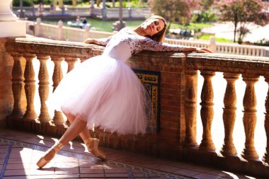 Beyaz tütü giymiş, parkın korkuluklarına yaslanmış güzel bir bale pozu veren klasik balerin. Klasik bale konsepti.
