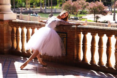 Beyaz tütü giymiş, parkın korkuluklarına yaslanmış güzel bir bale pozu veren klasik balerin. Klasik bale konsepti.