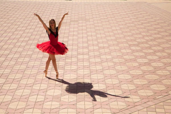 Classical ballet dancer dancing in the street. The dancer is wearing a red tutu and is performing a classical work from Spain, Carmen. You can see the shadows of the dancer on the floor. Classical ballet concept.