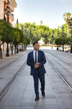 Genç, yakışıklı, koyu renk saçlı, takım elbiseli, kravatlı ve siyah dantelli ayakkabılı bir işadamı Seville 'de büyük bir caddede tramvay rayları arasında yürüyor. Adam çok uluslu bir şirketin yöneticisi.