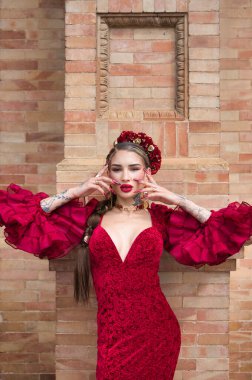 A beautiful woman dancing flamenco in a red ruffled dress leaning against the wall with her hands on her face and flamenco feeling. Flamenco, cultural heritage of humanity