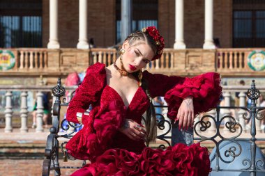 İspanya, Seville 'de bir meydanda fayanslı bir bankta dans eden güzel bir kadın. Kırmızı bir fırfırlı elbise, makyaj ve takma tırnaklar giyiyor. Flamenko, insanlığın kültürel mirası.