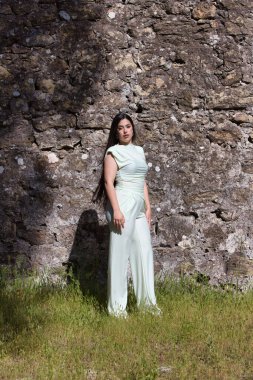 Uzun siyah saçlı güzel bir İspanyol genci, kentin dışındaki harabe bir şatonun taş duvarının yanındaki yeşil çimlerin üzerinde bir model gibi poz veriyor. Güzellik ve moda kavramı