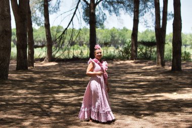 Geleneksel pembe ve beyaz flamenko elbiseler giymiş, saçları çiçekli genç bir İspanyol kadın hacca giderken Endülüs 'ün çam ağaçları arasında yürür.