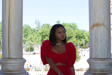 Afrikalı bir kadın, uzun kahverengi saçlı, genç ve güzel, Endülüs 'ün başkenti İspanya' da bulunan meydandaki iki beyaz mermer sütun arasında zarif kırmızı bir elbise giymiş.