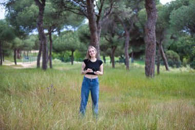 Genç ve güzel sarışın kadın, kot giyen, siyah gömlekli ağaçlar ve çiçekler arasında tarlada yürüyen. Kadın yalnızlığın ve ormanın bahar gününün tadını çıkarıyor.
