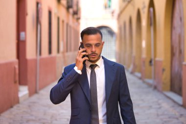 Genç, yakışıklı, koyu renk saçlı, takım elbiseli, kravatlı ve siyah dantelli ayakkabılı bir iş adamı telefonda ciddi bir ifadeyle konuşuyor. Adam çok uluslu bir şirketin yöneticisi.