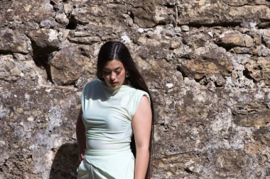 Uzun siyah saçlı güzel bir İspanyol genci, kentin dışındaki harabe bir şatonun taş duvarının yanındaki yeşil çimlerin üzerinde bir model gibi poz veriyor. Güzellik ve moda kavramı