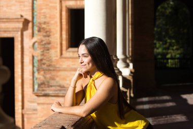 Genç, güzel, koyu renk saçlı, kırmızı elbiseli bir İspanyol kadın Sevilla 'daki Plaza İspanya' daki çeşmesinin önüne atlıyor. Arka planda, su bir gökkuşağı oluşturur.