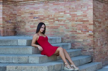 Genç, güzel, koyu renk saçlı, kırmızı elbiseli bir İspanyol kadın Sevilla 'daki Plaza İspanya' daki çeşmesinin önüne atlıyor. Arka planda, su bir gökkuşağı oluşturur.