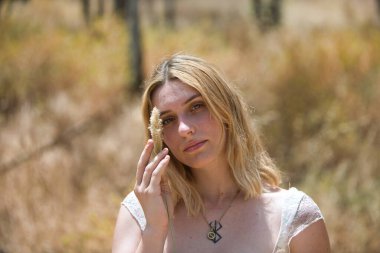 Genç, güzel sarışın bir kadının portresi. Huzurlu bir bakışla elinde kuru, yumuşak bir mısır kabuğu tutuyor ve narinlik ve şefkat ile yüzünün yanına yerleştiriyor.