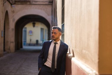 Genç, yakışıklı, koyu renk saçlı, takım elbiseli ve kravatlı bir iş adamı, ciddi bir ifadeyle duvara yaslanmış, sigara içiyor. Adam çok uluslu bir şirketin yöneticisi.