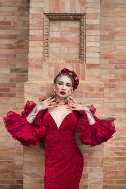 A beautiful woman dancing flamenco in a red ruffled dress leaning against the wall with her hands on her face and flamenco feeling. Flamenco, cultural heritage of humanity