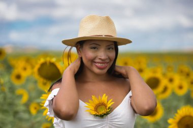 Beyaz gömlek ve hasır şapka giyen koyu tenli genç bir Latin kadın çiftçinin portresi ayçiçeklerinin arasında duruyordu. Kız elleriyle saçlarını tutuyor ve göğsüne bir ayçiçeği sıkıştırıyor.