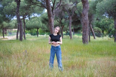 Genç ve güzel sarışın kadın, kot giyen, siyah gömlekli ağaçlar ve çiçekler arasında tarlada yürüyen. Kadın yalnızlığın ve ormanın bahar gününün tadını çıkarıyor.