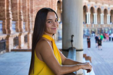 Genç, güzel, koyu renk saçlı, kırmızı giyinmiş İspanyol bir kadın Sevilla 'daki İspanya Meydanı' ndaki çeşmenin önüne atlıyor. Arka planda, su bir gökkuşağı oluşturur.