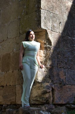 Uzun siyah saçlı güzel bir Latin genç şehrin dışındaki terk edilmiş bir kalenin taşlarına poz veriyor. Kadın farklı pozlar ve ifadeler veriyor.