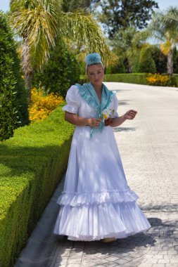 Saçında çiçekle geleneksel beyaz Endülüs flamenko elbisesi giymiş güzel bir İspanyol kadın. Kadın eline sarı bir çiçek aldı ve fotoğraf için poz verdi.