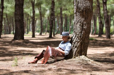 Genç, güzel bir kadın at kıyafetleri ve binicilik kıyafetleri giyer ve tipik bir İspanyol şapkası İspanya 'da kutsal bir günde bir çam ağacının gölgesinde dinlenir.