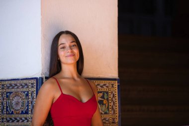 Genç, güzel, koyu renk saçlı, kırmızı giyinmiş, Sevilla Plaza de Espaa 'daki bir köprünün seramik korkuluklarına yaslanmış bir İspanyol kadın. Arka planda, anıtın bir kulesi.