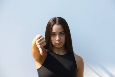 Siyah gömlekli bir kadın beyaz arka planda baş parmak hareketi yapıyor.