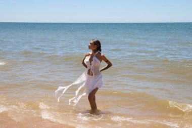 Güneşli bir yaz gününde beyaz giyinmiş güzel bir kadın denizden çıkıyor. Kadının elleri arkada ve Endülüs, İspanya 'da Huelva' da bir plajda duruyor.