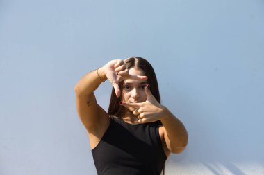 Günlük giysiler içinde gülümseyen, mutlu yüzüyle elleri ve parmaklarıyla bir çerçeve yapan genç insan. Yaratıcılık ve fotoğrafçılık kavramı