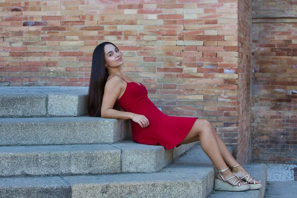 Genç, koyu renk saçlı, çekici Latin bir kadın sarı gömlek ve siyah pantolon giyiyor Seville 'deki Plaza de İspanya' nın korkuluklarında oturuyor sırtı mermer bir sütuna yaslanmış.