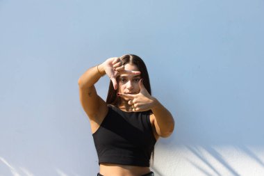 Günlük giysiler içinde gülümseyen, mutlu yüzüyle elleri ve parmaklarıyla bir çerçeve yapan genç insan. Yaratıcılık ve fotoğrafçılık kavramı