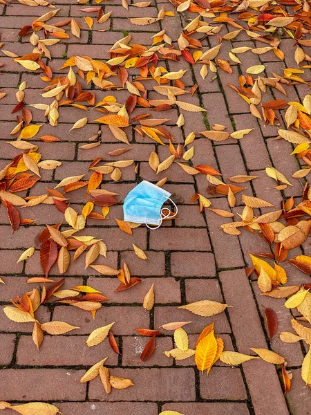 Sonbahar yaprakları arasında tuğla kaldırıma atılmış kullanılmış bir tıbbi maske..