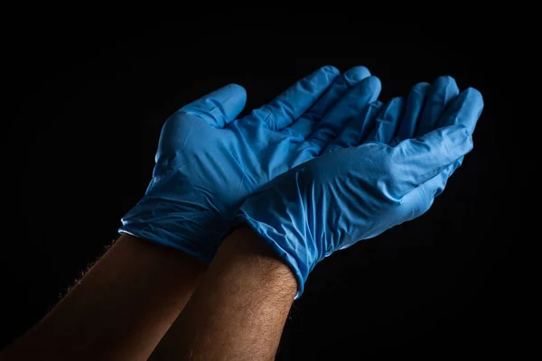 Palms in blue, latex gloves asking for help on a black background.