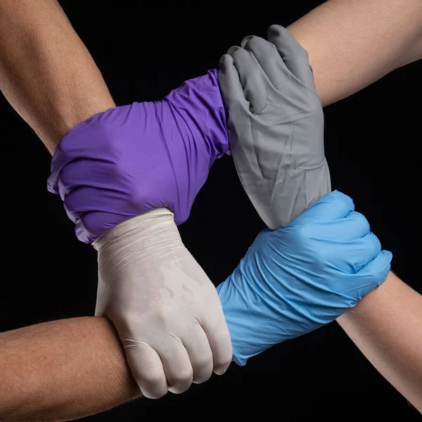 Farklı renklerde lateks eldivenli adamlar, siyah bir arka planda el ele tutuşuyorlar..