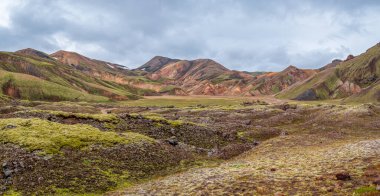 Colorful rhyolite hills and mossy lava fields in Iceland under dramatic cloudy sky.