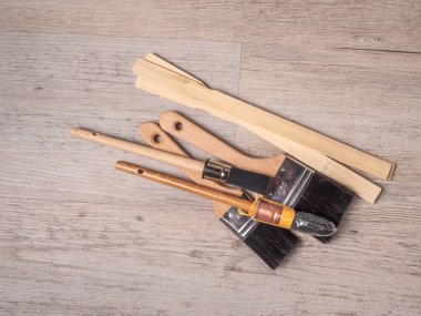 Bir yığın çeşitli boya fırçaları ve ahşap karıştırma çubukları açık gri-kahverengi ahşap yüzey üzerinde durmaktadır.