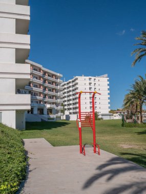 Beyaz otel binaları ve çimlerle çevrili kırmızı spor aletleri olan spor salonu..